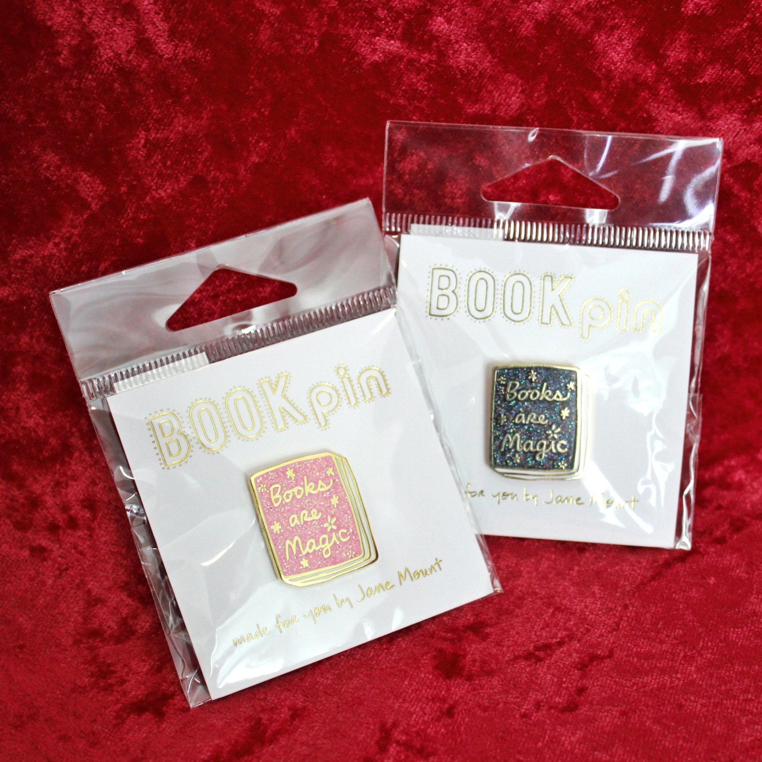 2 inch metallic gold pins with a book cover design; "Books Are Magic" in script font. Available in pink or black.